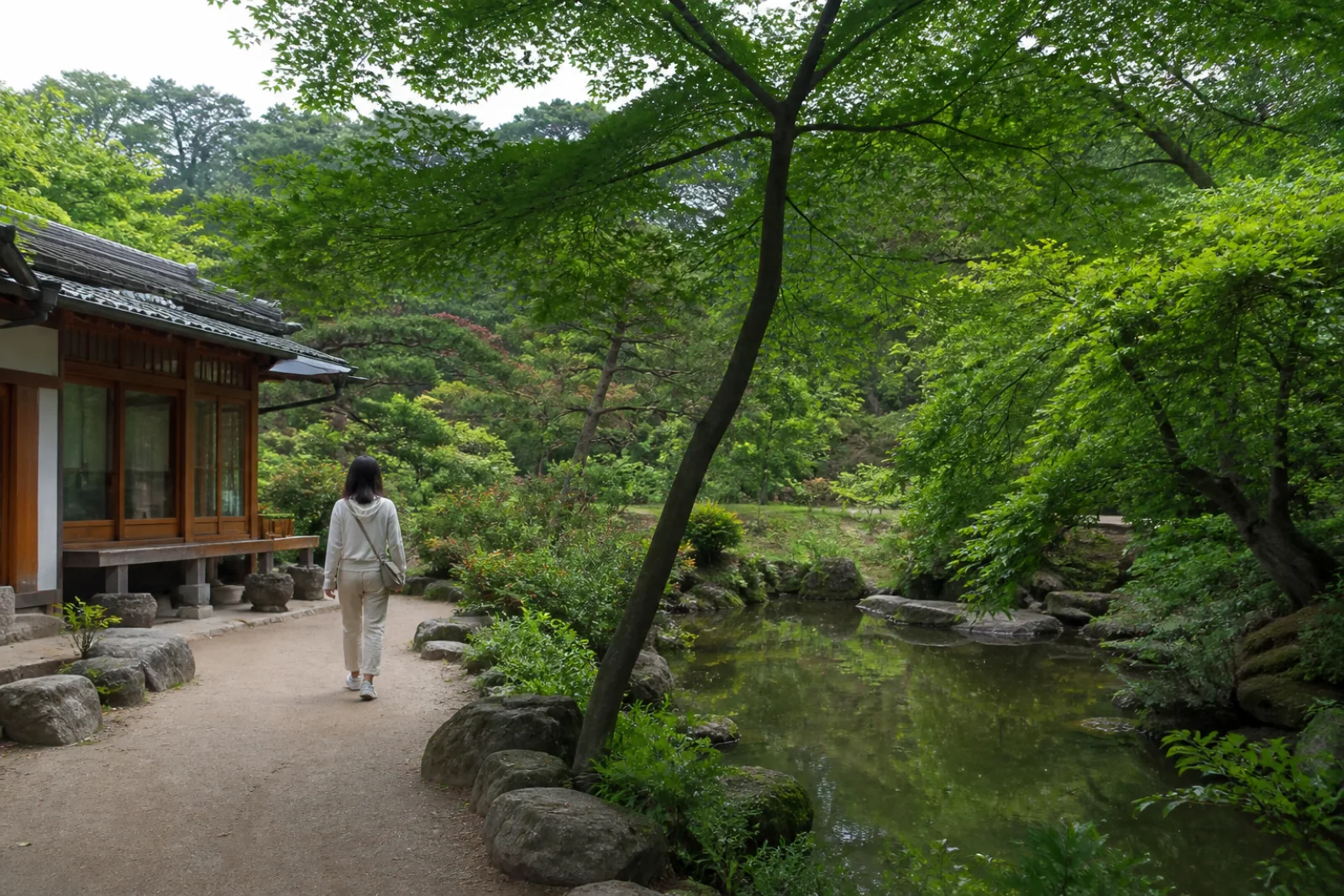 A visitor walking a quiet garden path beside a pavilion and natural slope in Korea