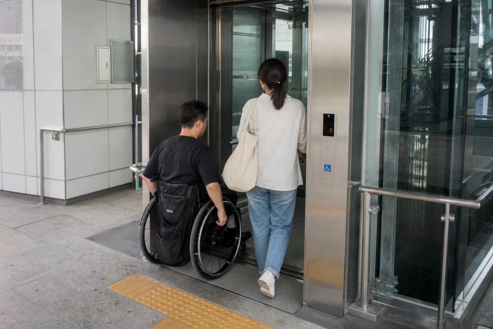 A wheelchair user and friend entering a bright modern Seoul transit elevator