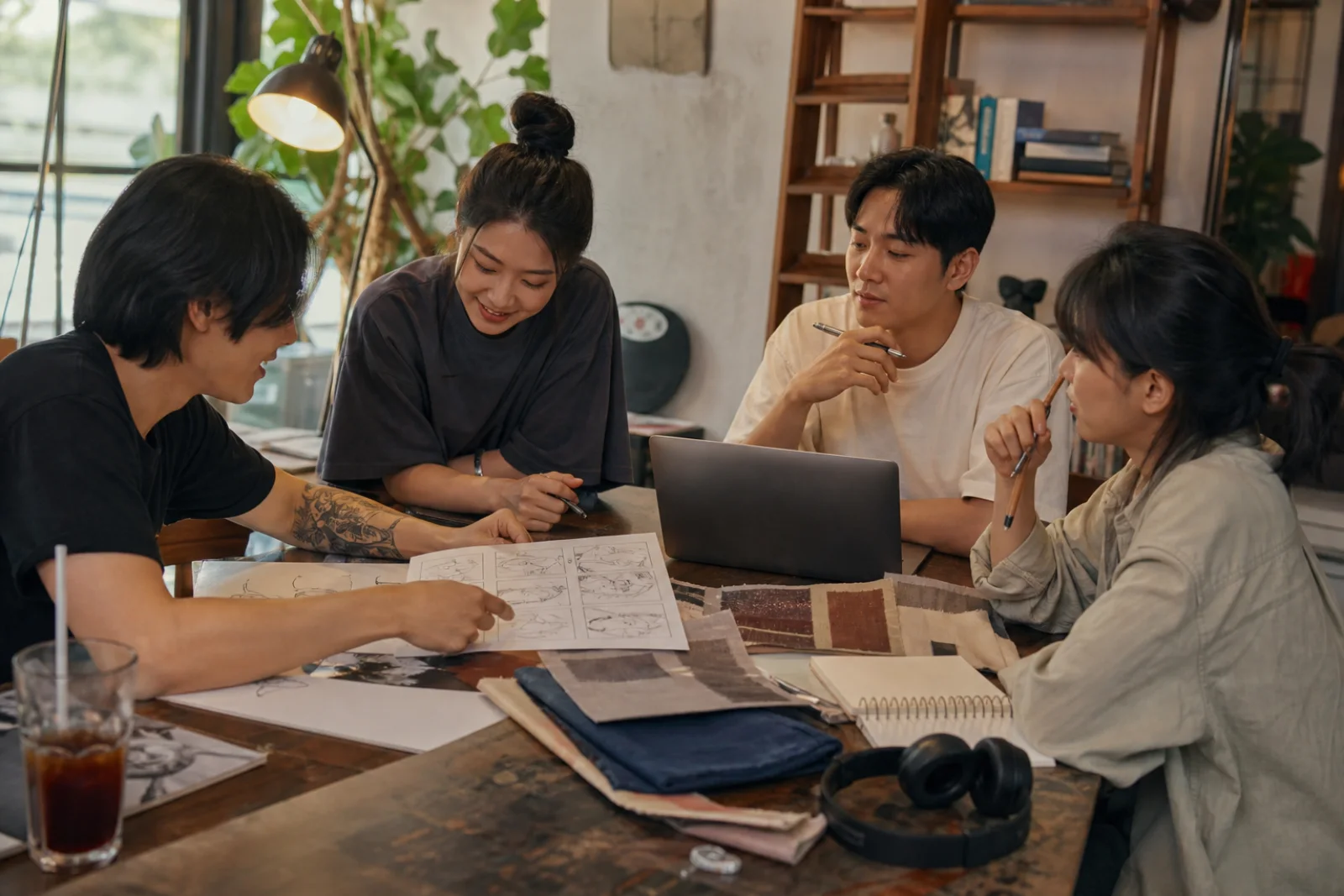 A mixed group of young Korean creators sharing work around a studio table