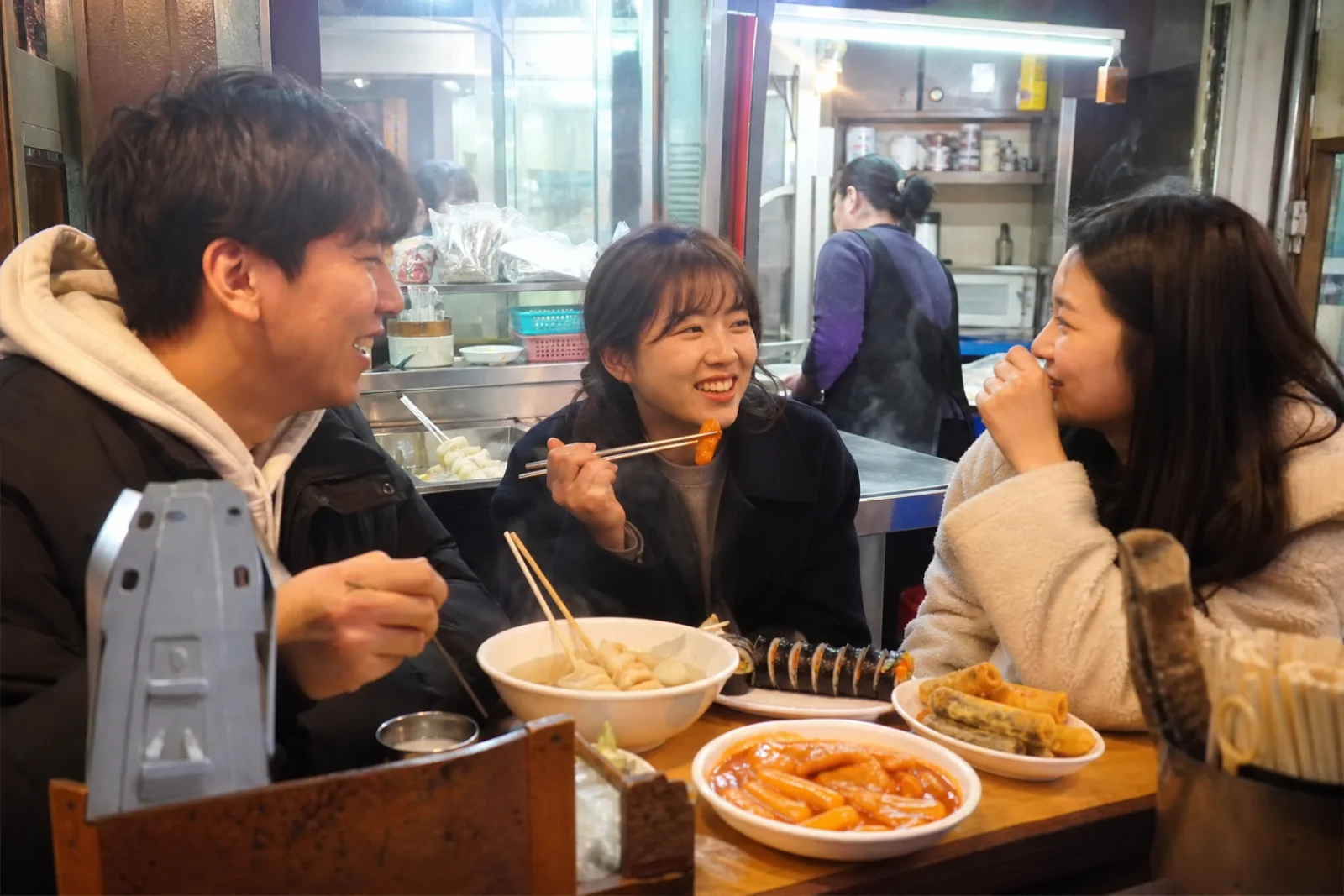 Students sharing tteokbokki and gimbap at a small Korean snack counter