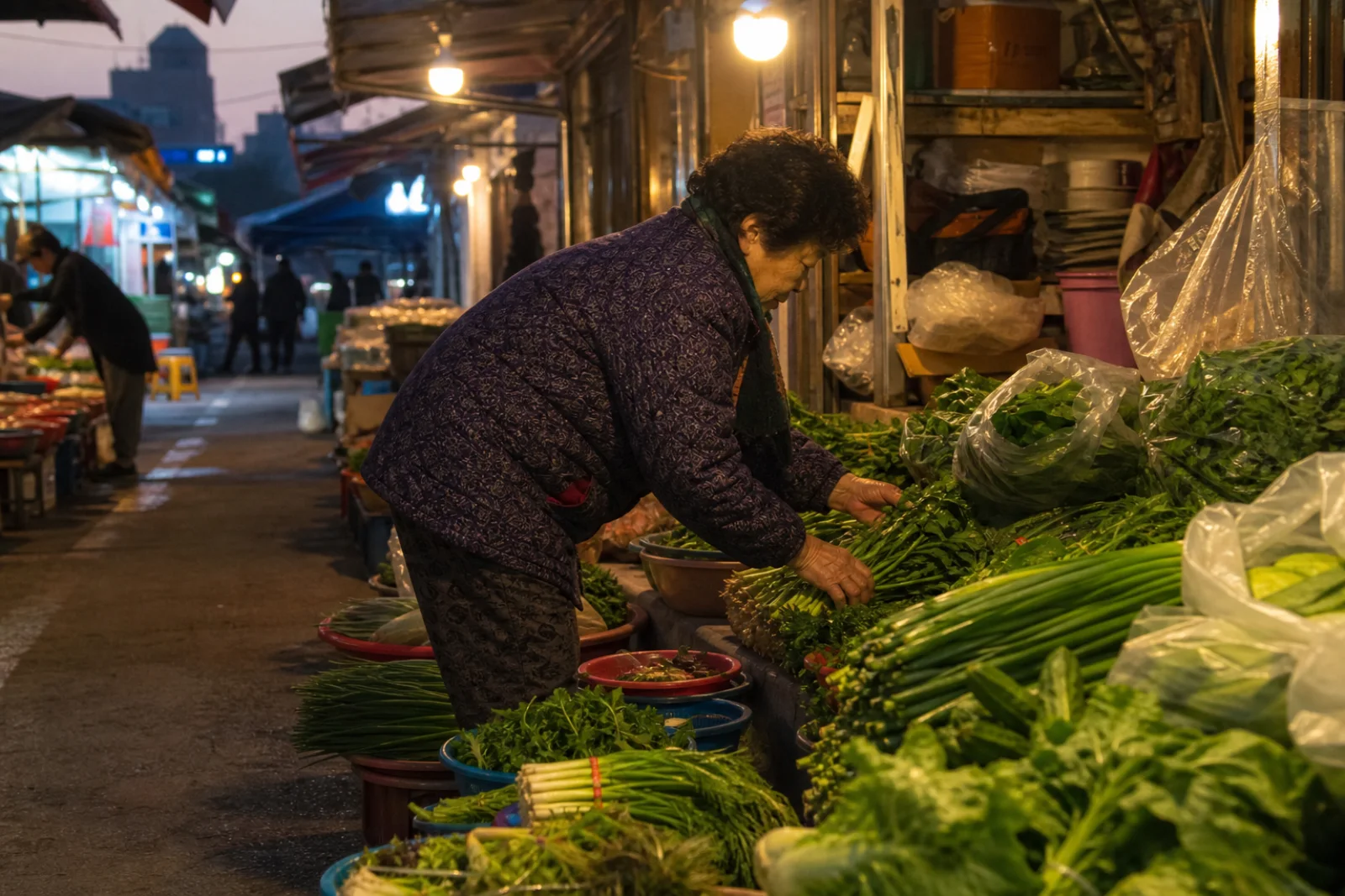 A Korean market vendor arranging vegetables in soft light before opening