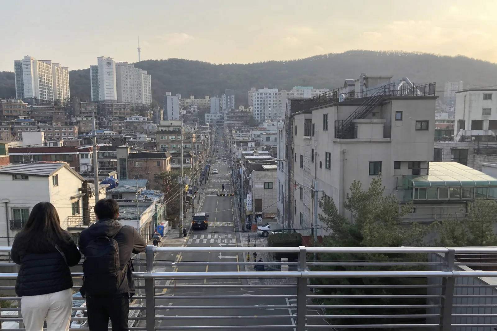 An everyday Seoul neighborhood seen from a footbridge with hills and mixed buildings