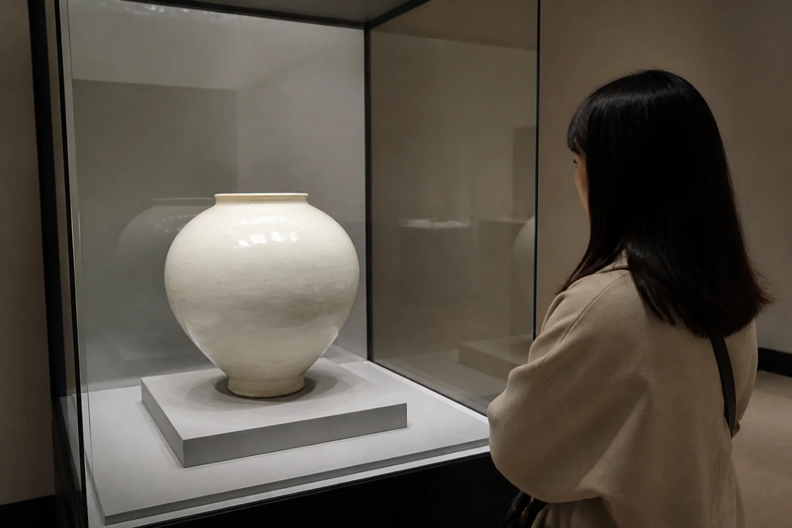 A museum visitor looking at a moon jar from the side in a quiet gallery