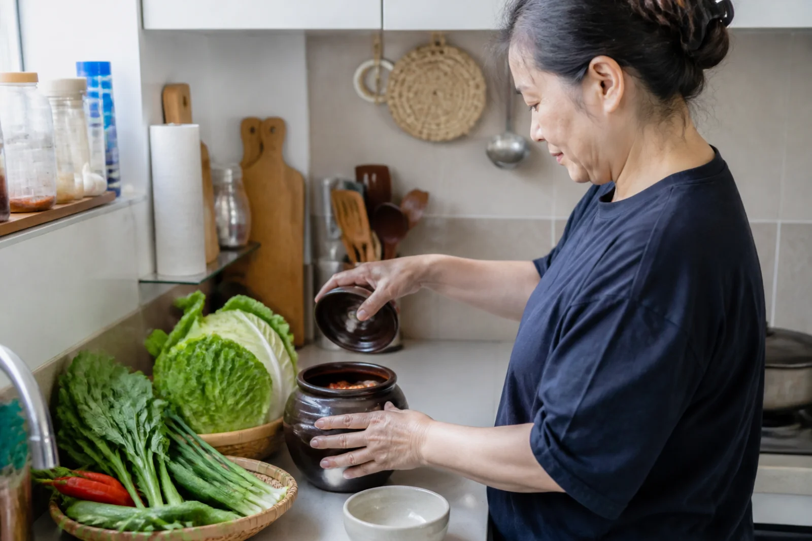 A cook checking a small onggi jar and vegetables in a contemporary Korean kitchen