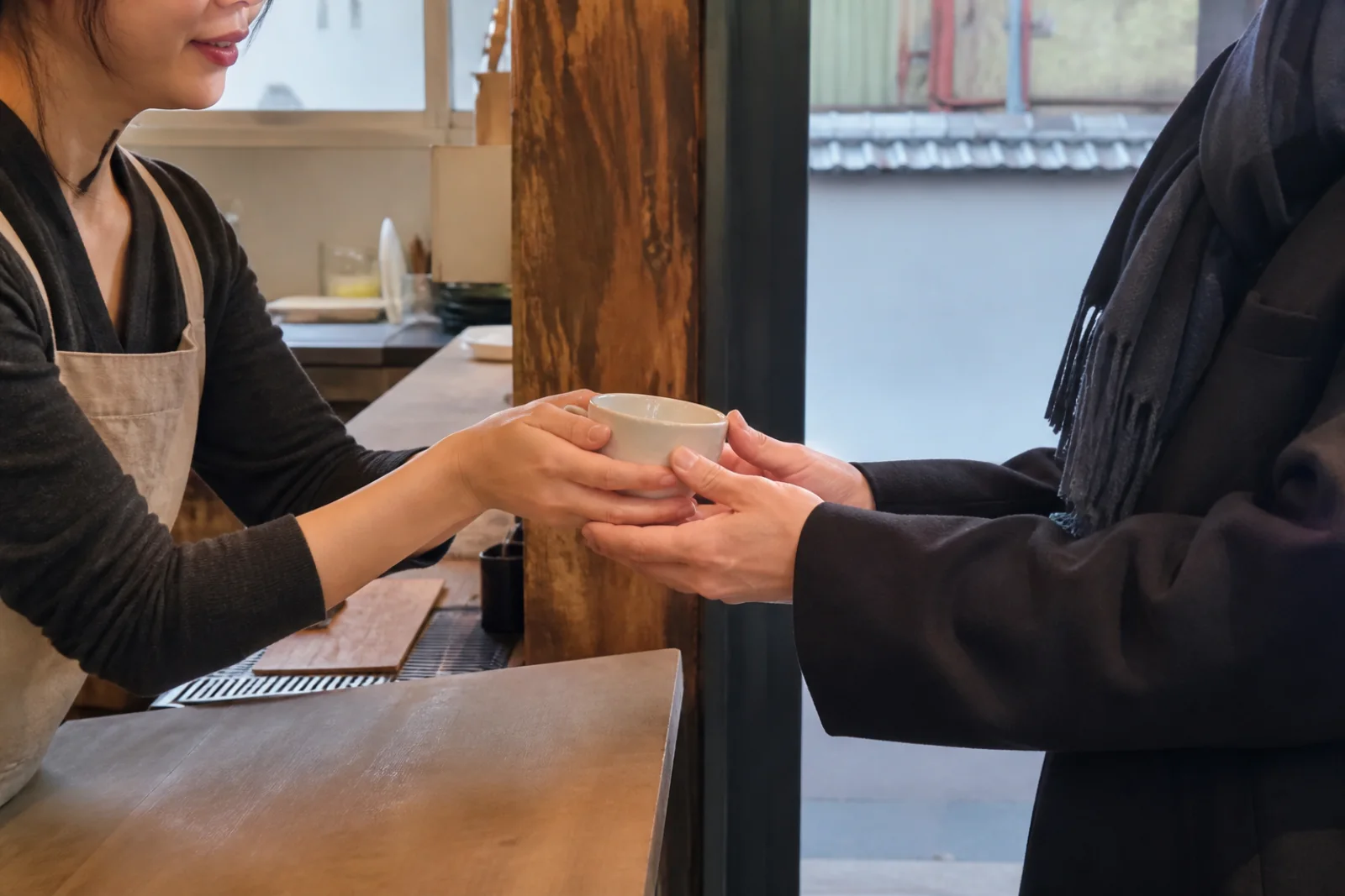 A cafe worker and customer exchanging a small item with both hands