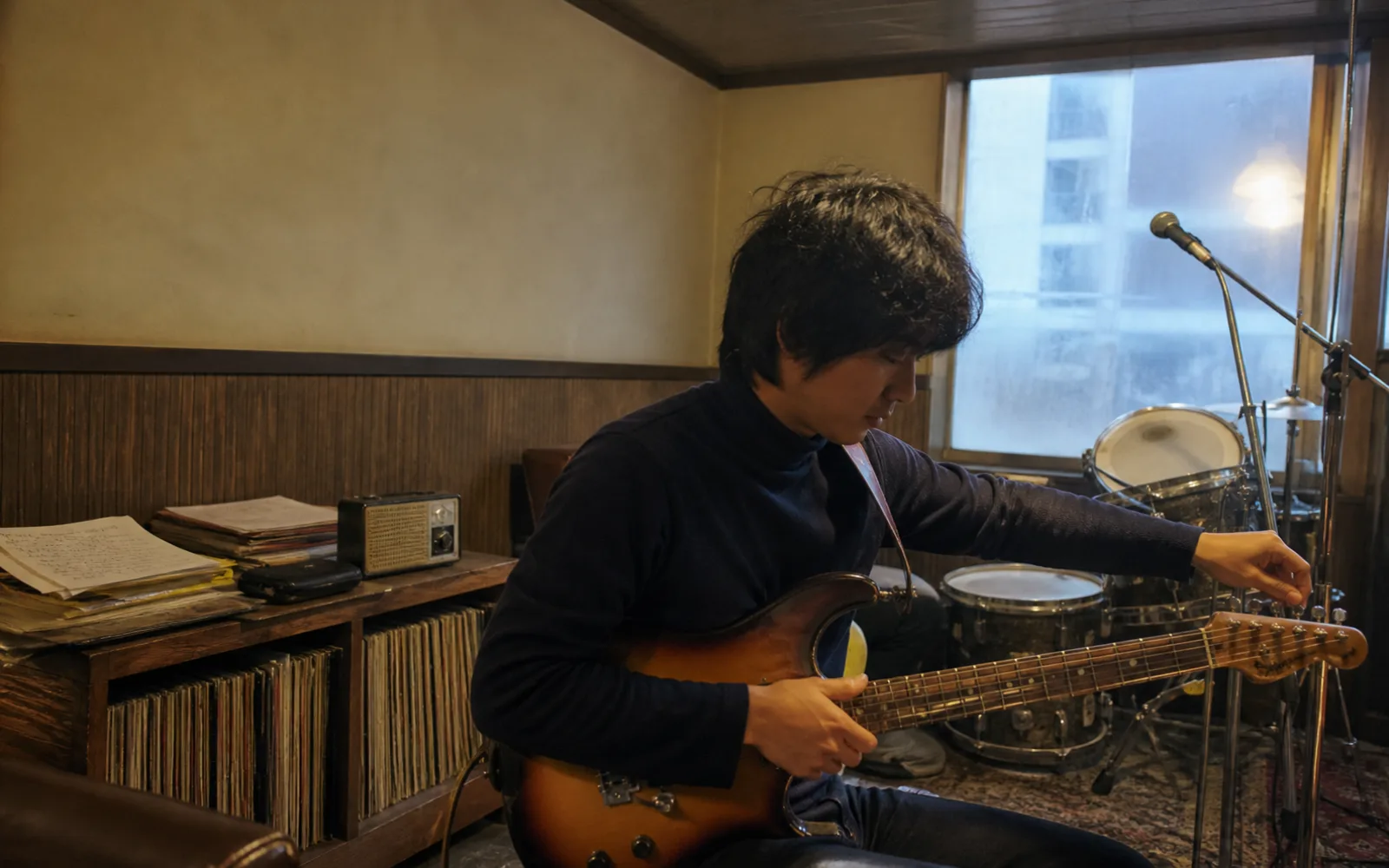 Editorial reconstruction of a Korean musician tuning a guitar in a late-1970s rehearsal room