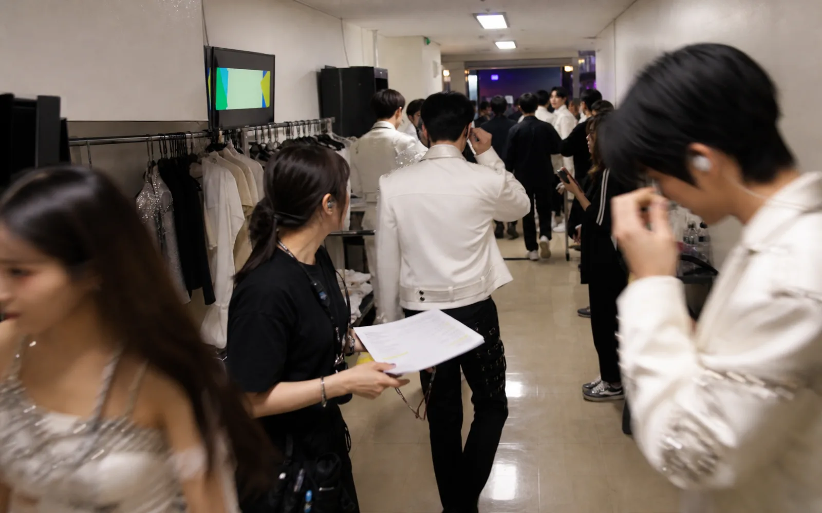 Generic performers and crew moving through a Korean broadcast-station corridor before a music show
