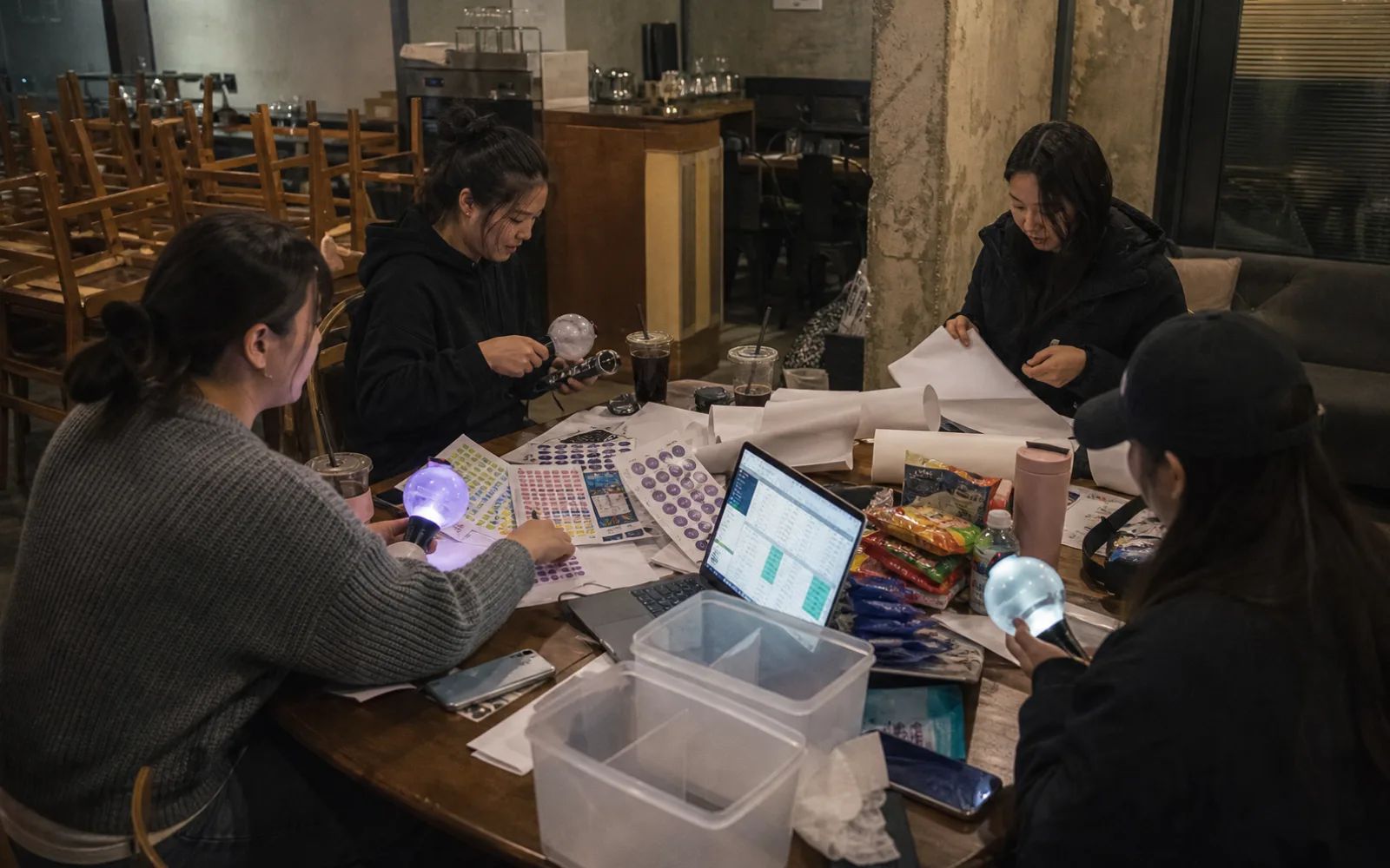 Adult fans preparing generic light sticks, blank banners, and translation notes in a cafe