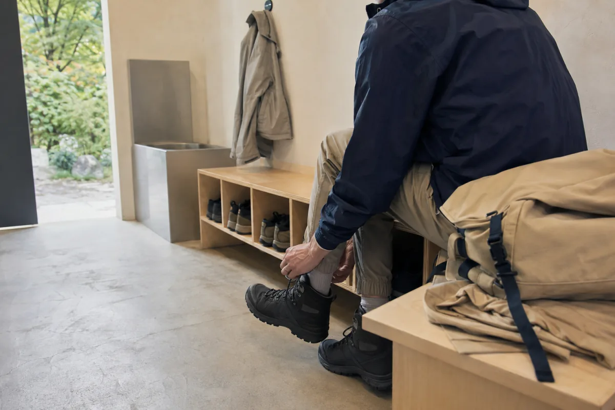 A fictional adult visitor tightens plain hiking boots in a generic gear-preparation lounge