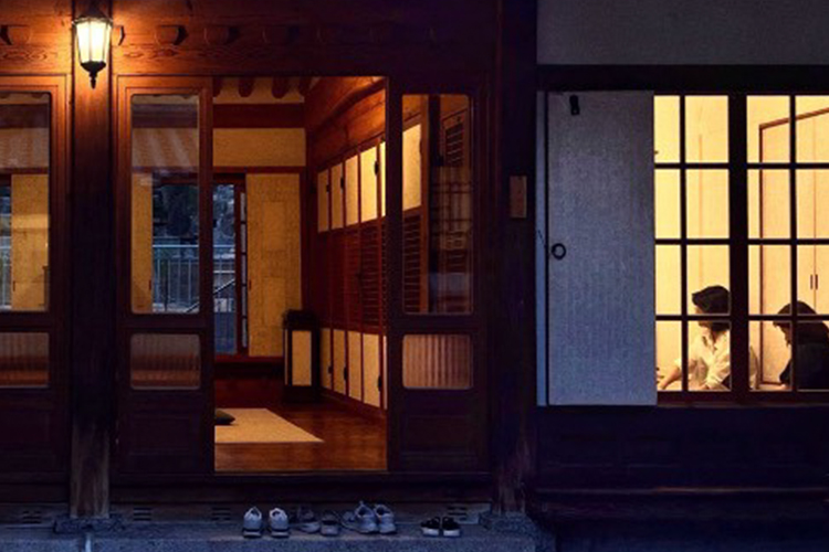 Exterior of Hong Geonik House at night, with visitors seated behind softly lit paper doors