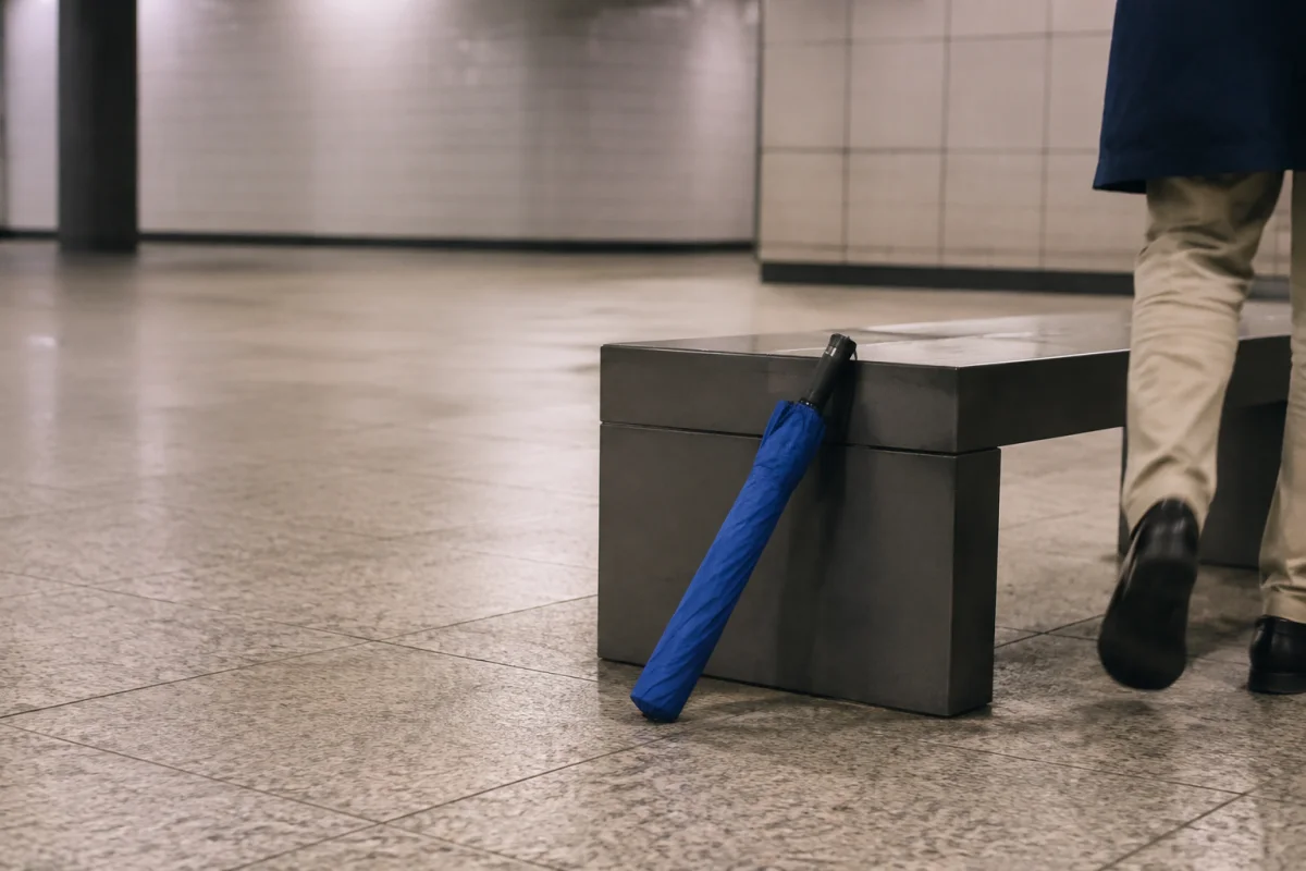 A plain blue umbrella rests against an unbranded subway concourse bench as an anonymous adult walks away