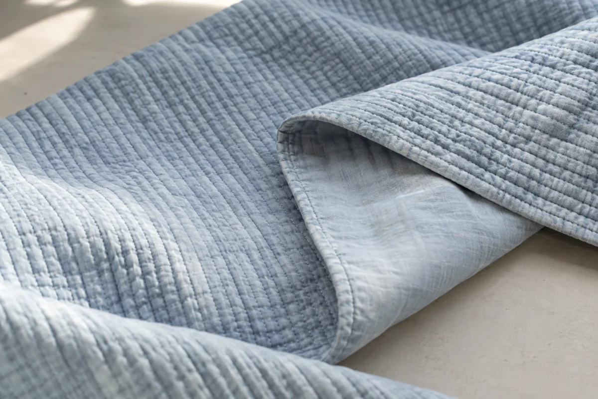 A folded pale blue quilted cloth with fine parallel stitching and a plain backing in side light.