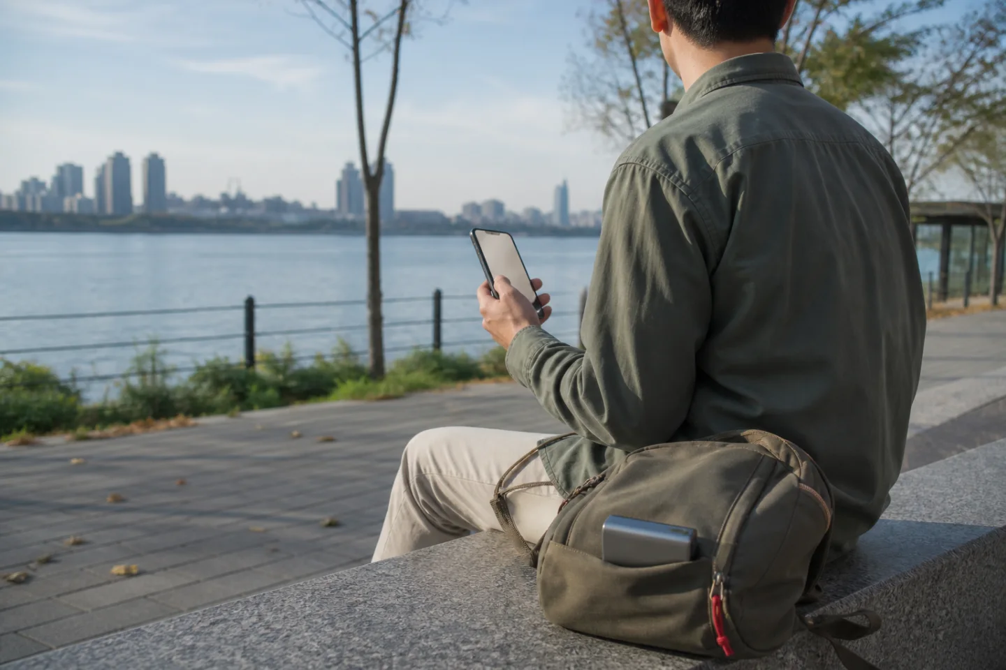 AI-generated editorial view of an anonymous adult checking an unbranded phone beside a daypack in a generic Seoul-like riverside park