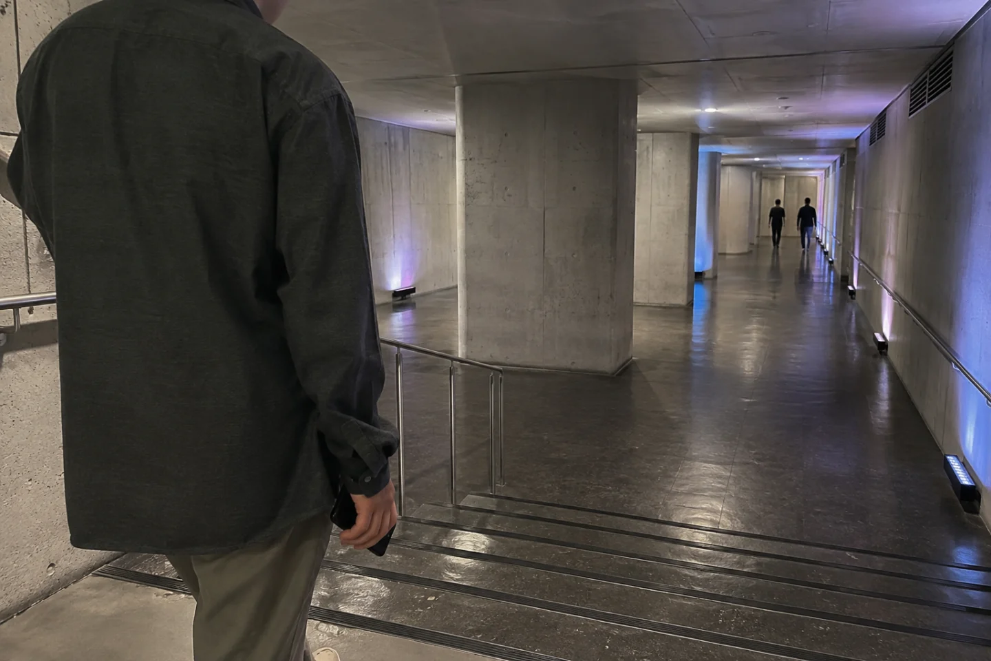 AI-generated editorial view of an anonymous visitor entering a fictional concrete underground culture corridor